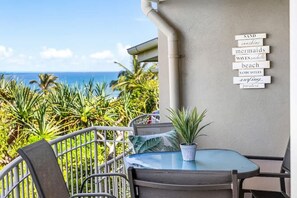 A balcony with a view of the ocean, a table with chairs, and a sign with words like 'beach' and 'mermaids'. - 3 Andari Sunshine Beach Modern Apt 1 Min Beach (Noosa)
