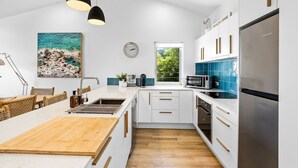 Una cocina moderna con armarios blancos, una mesa de comedor de madera, luces colgantes, un reloj y vistas a zonas verdes.