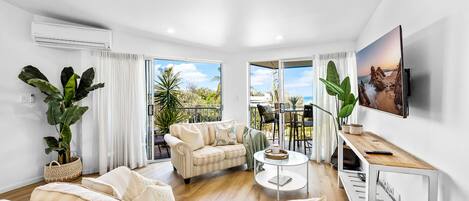 A spacious living room with a sofa, coffee table, and a TV mounted on the wall.