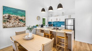 Una cocina moderna con armarios blancos, un refrigerador de acero inoxidable y un comedor con mesa de madera y sillas de mimbre.