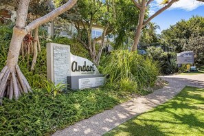 A sign for Andari Holiday Apartments with a landscaped garden and a pathway.