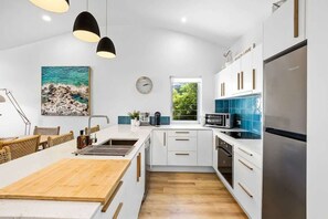 A modern kitchen with white cabinetry, a wooden island, a stainless steel refrigerator, and pendant lighting.