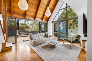 A spacious living room with a high ceiling, large windows, a sofa, a coffee table, and a chair.