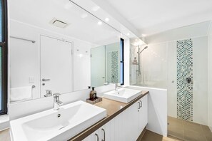 A modern bathroom with two sinks, a large mirror, and a shower with a glass door.