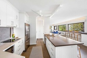 Une cuisine moderne avec des meubles blancs, un grand îlot central et une vue par la fenêtre.