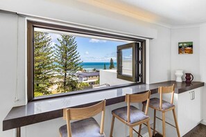 Un balcon avec vue sur la mer, un coin bar avec des tabourets et un intérieur blanc.