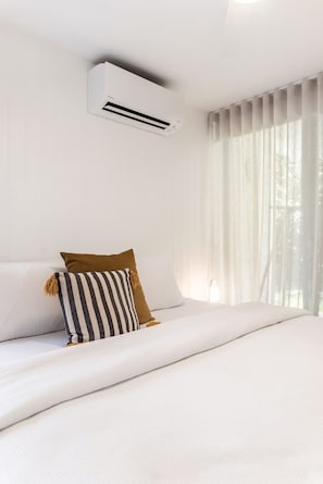 Quarto de hotel com cama, cortinas brancas e aparelho de ar condicionado.