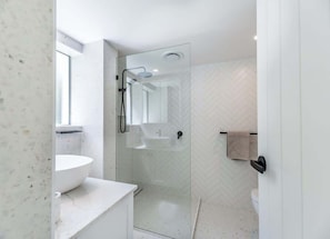 Uma casa de banho moderna com cabine de duche em vidro, lavatório branco e parede com padrão herringbone.