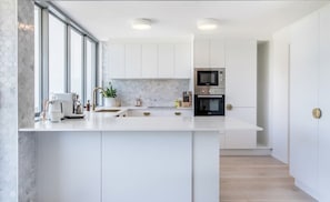 Cozinha moderna com armários brancos, uma ilha central, micro-ondas e forno.