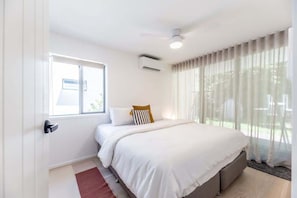 A hotel room with a bed, a window, a door, and a ceiling fan. - Sunrise Central Pool Views 1 Min to Beach (Sunrise Beach)