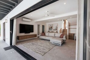 Una sala de estar moderna con un televisor de pantalla plana, un sofá, una mesa de centro y un ventilador de techo.