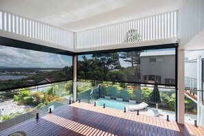 A modern balcony with a glass railing, a pool, and a view of a natural landscape.