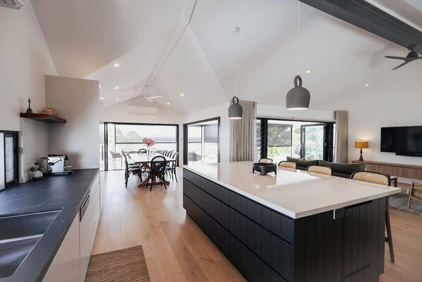 A modern kitchen with a large island, dining area with chairs, and a TV mounted on the wall.