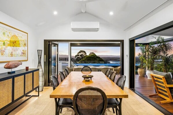 Un comedor con vistas a un cuerpo de agua y colinas, un cuadro grande en la pared y un equipo moderno de aire acondicionado.