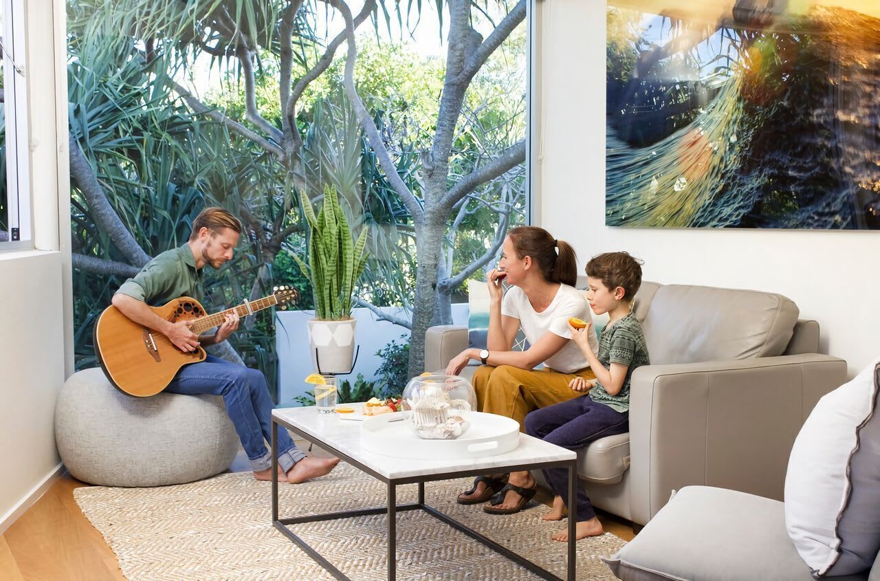 A room with a large window, a sofa, a coffee table, and a guitar player.