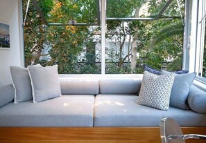 A modern living room with a grey sofa, patterned pillows, and a view of trees through large windows.