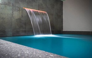 A pool with a waterfall feature, surrounded by tiled walls.