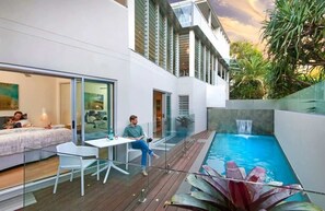 A modern outdoor living area with a pool, glass doors, and a dining table.