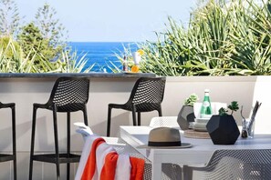 A terrace with two black mesh chairs, a white table, and a view of the ocean.