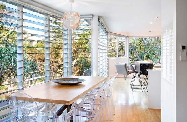 A modern dining area with a wooden table, clear chairs, and a large window with a view of greenery.