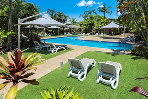 A pool area with lounge chairs and umbrellas, surrounded by tropical vegetation.