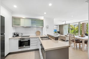 A modern kitchen with a built-in oven, a coffee maker, and a large window overlooking a garden. - Beautiful Apt in Luxe Beachside Noosa Resort (Noosa)