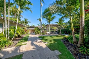 A pathway leading to a building with a covered patio area, surrounded by palm trees and well-maintained grass.