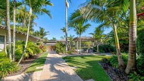 A pathway leading to a covered outdoor area with palm trees and a building with a tiled roof. - Beautiful Apt in Luxe Beachside Noosa Resort (Noosa)