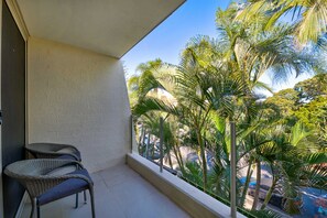 A balcony with a view of palm trees and a parked car.