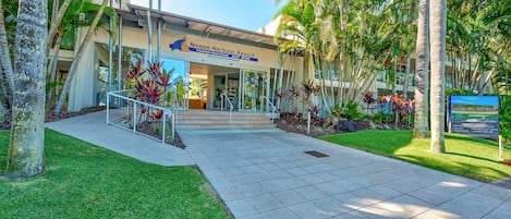 Entrada a un resort con un cartel que dice Noosa Harbour Resort, con un camino pavimentado, palmeras y un césped bien cuidado.