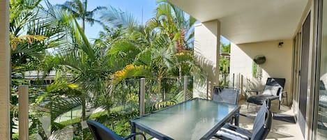 Un balcón con una mesa y sillas de vidrio, rodeado de exuberante vegetación tropical.