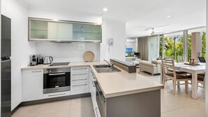 A modern kitchen with a built-in oven, a coffee maker, and a large window overlooking a garden. - Beautiful Apt in Luxe Beachside Noosa Resort (Noosa)