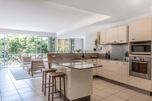 Eine moderne Küche mit einer großen Kochinsel, Edelstahlgeräten und einem Balkon mit Sitzgelegenheit.