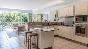 A modern kitchen with a large island, stainless steel appliances, and a balcony with seating. - Heart of Sunshine Spacious Apt Pool and Garden (Noosa)
