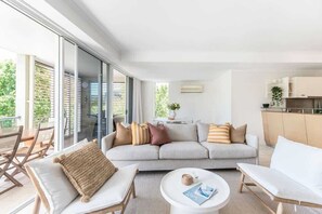 Ein modernes Wohnzimmer mit einer Couch, zwei Sesseln, einem Couchtisch und einer Schiebetür zu einem Außenbereich.