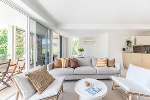 A modern living room with a sofa, chairs, a coffee table, and a view of the outdoors through large glass doors. - Heart of Sunshine Spacious Apt Pool and Garden (Noosa)