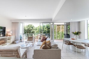 A modern living room with a sofa, chairs, a dining table, and a TV. - Heart of Sunshine Spacious Apt Pool and Garden (Noosa)