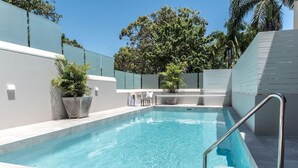 A rectangular swimming pool with clear blue water, surrounded by a white wall and a green fence. - Heart of Sunshine Spacious Apt Pool and Garden (Noosa)