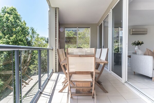 Ein Balkon mit Tisch und Stühlen, eine Schiebeglastür und ein weißes Sofa.