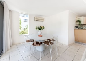 A modern dining area with a round table, white chairs, and a vase of flowers. - Heart of Sunshine Spacious Apt Pool and Garden (Noosa)