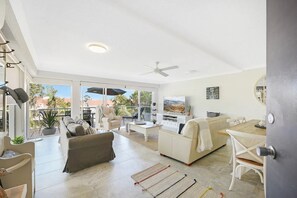 Relax in this spacious living area with a high ceiling, ceiling fan, and sliding glass door leading to an outdoor patio with dining and seating areas.