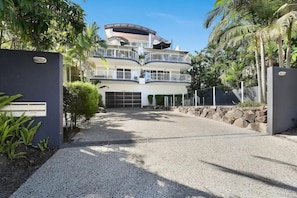 A multi-story building with balconies, a gated entrance, and a gravel driveway.