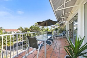 Enjoy the view from this balcony with a glass table and chairs, surrounded by a potted plant and a white fence.