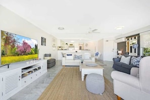 Ein modernes Wohnzimmer mit Flachbildfernseher, einer Couch, einem Couchtisch und einem Essbereich im Hintergrund.
