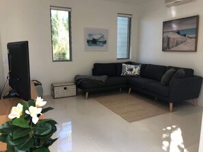 Ein modernes Wohnzimmer mit einer Eckcouch, einem Flachbildfernseher und einem großen Fenster, das für natürliches Licht sorgt.