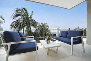 Ein moderner Außenbereich mit zwei Sofas und Sesseln, einem kleinen Tisch und Blick auf Palmen und den Himmel.