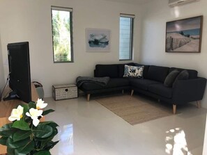 A living room with a black sofa, a plant, and artwork on the walls. - Coastal Chic with Heated Pool Quiet Location (Noosa)