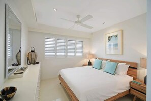 A bedroom with a bed, bedside tables, a ceiling fan, a large mirror, and a window with blinds. - Coastal Chic with Heated Pool Quiet Location (Noosa)