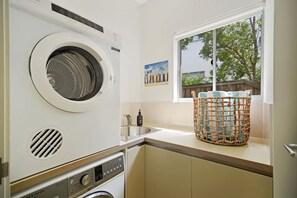 A laundry room with a front-loading washing machine, a dryer, a sink, and a window with a view of trees.