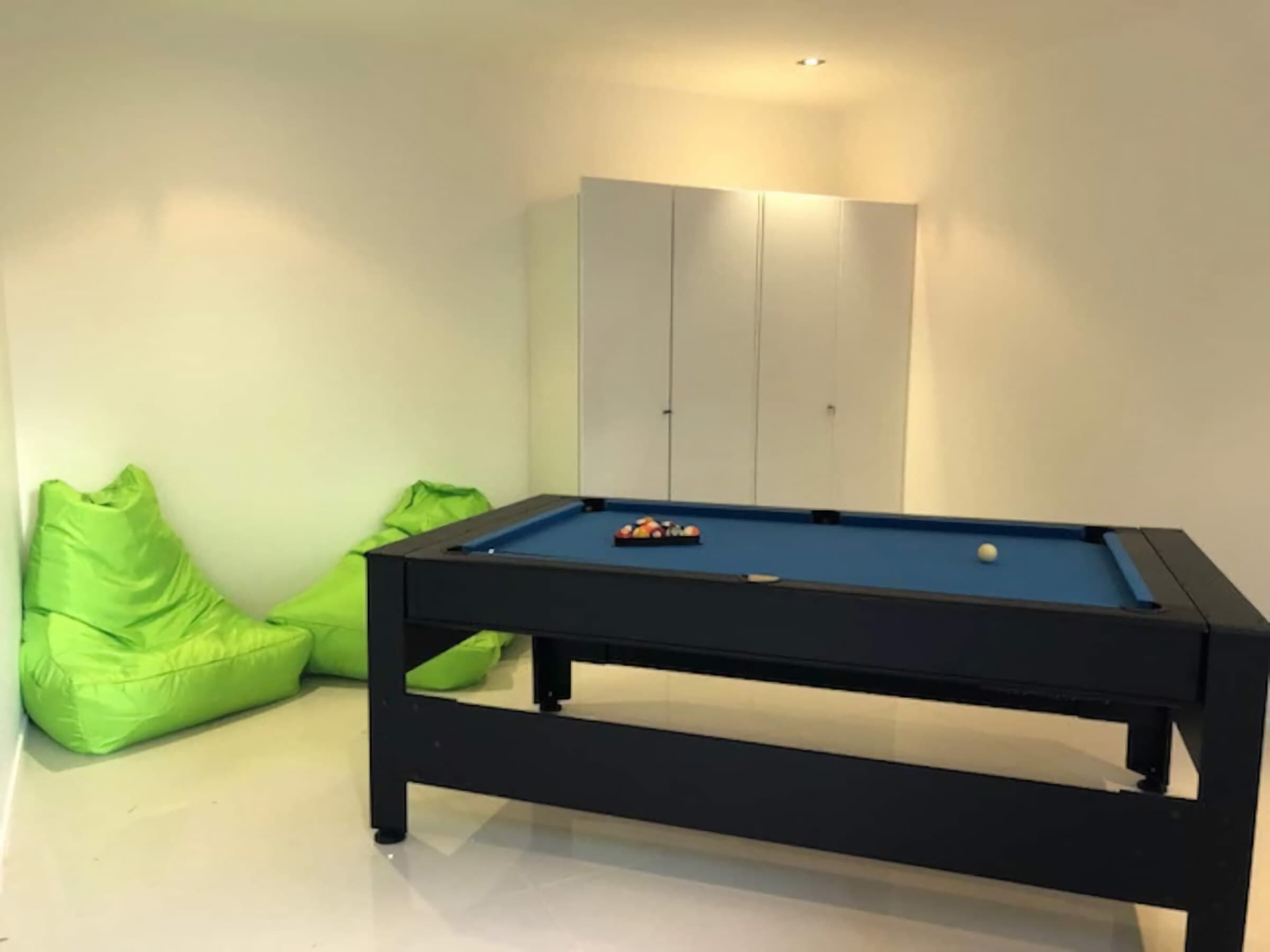 Ein Billardtisch mit Kugeln, grüne Sitzsäcke und ein Schrank.